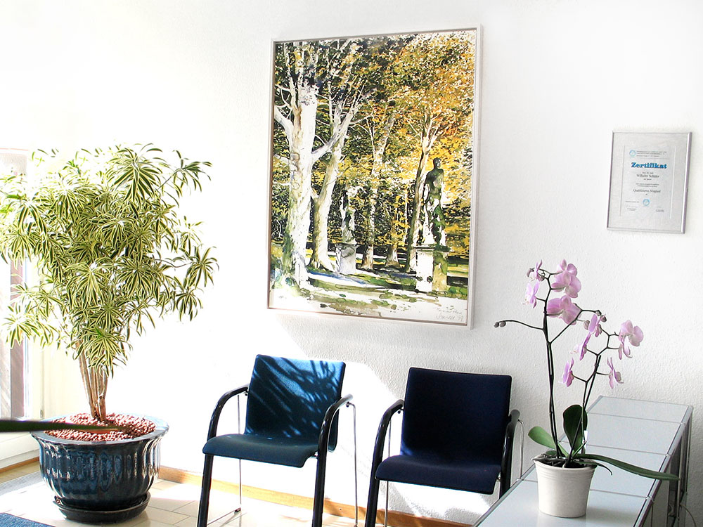 Wartezimmer mit zwei blauen Stühlen, einer großen Zimmerpflanze, einer Orchidee und einem gerahmten Gemälde an der Wand. Ein Zertifikat hängt daneben.
